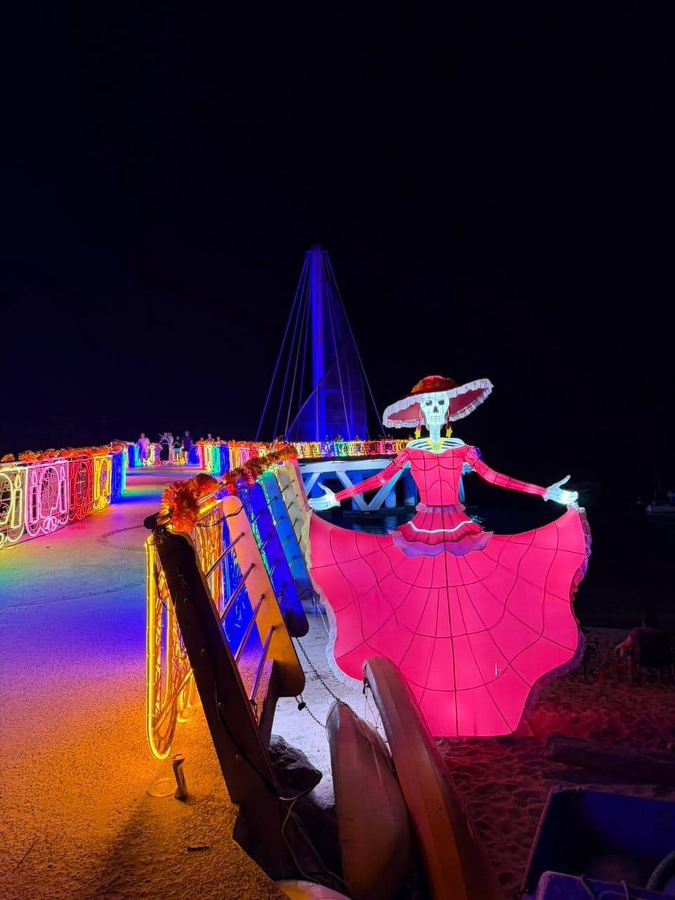 A giant illuminated Catrina in a red dress on the pier at night for Día de Muertos