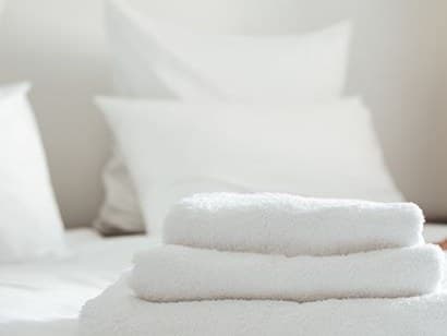 Una pila de toallas blancas limpias sobre una cama recién tendida con almohadas blancas