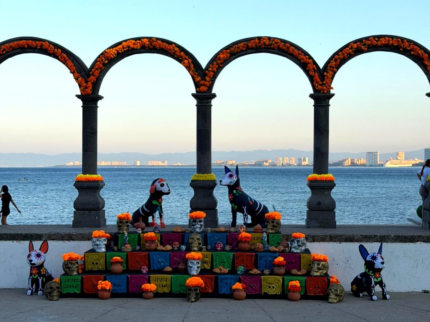 Los arcos del Malecón adornados con cempasúchil, un altar de Día de Muertos al frente y la bahía detrás