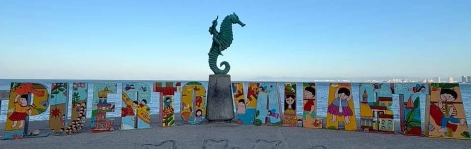 Las letras pintadas de Puerto Vallarta y la estatua de bronce del caballito de mar en el Malecón, con la bahía detrás